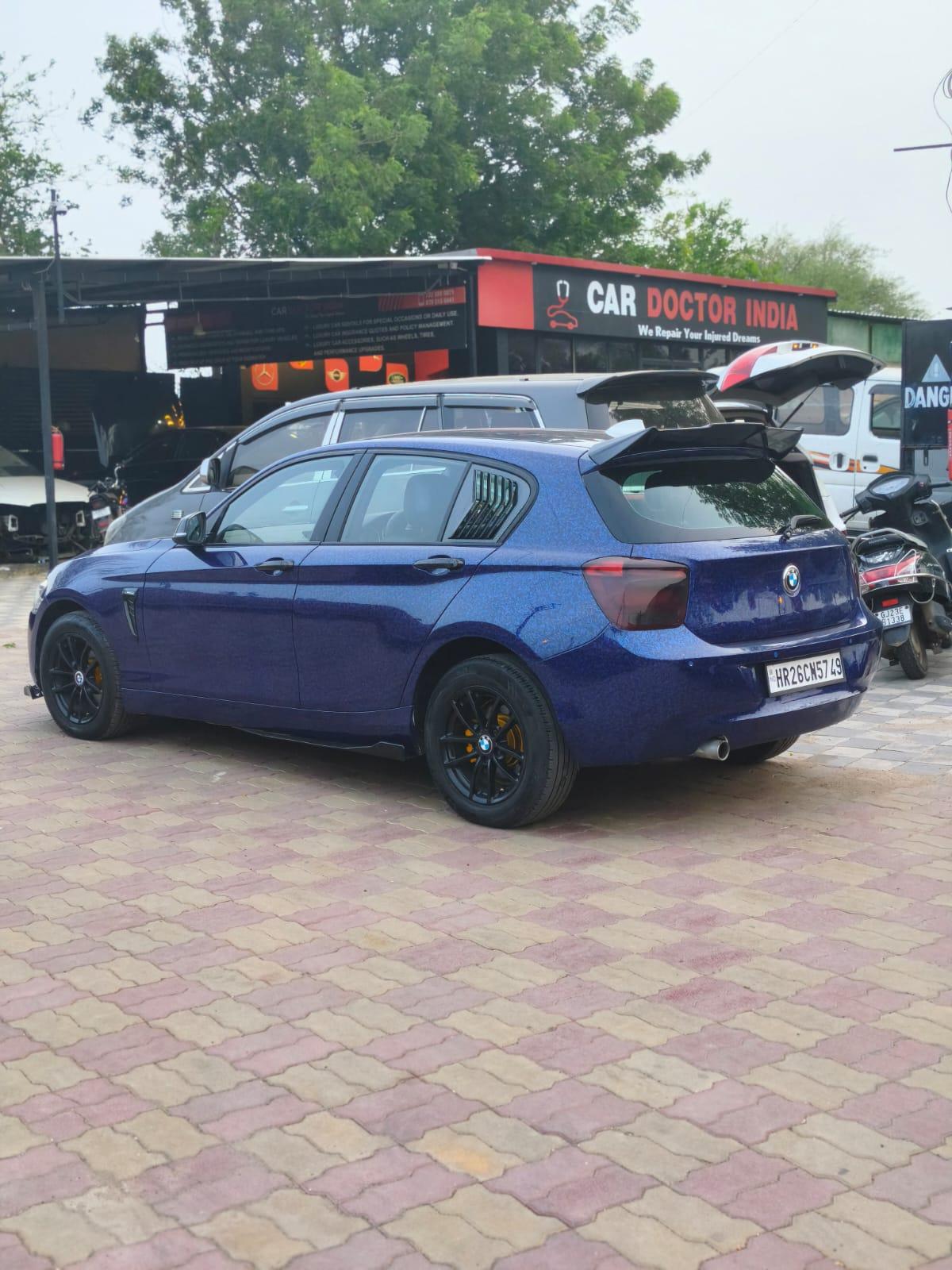 A blue BMW 1 Series with black alloy wheels parked outside the Car Doctor India workshop