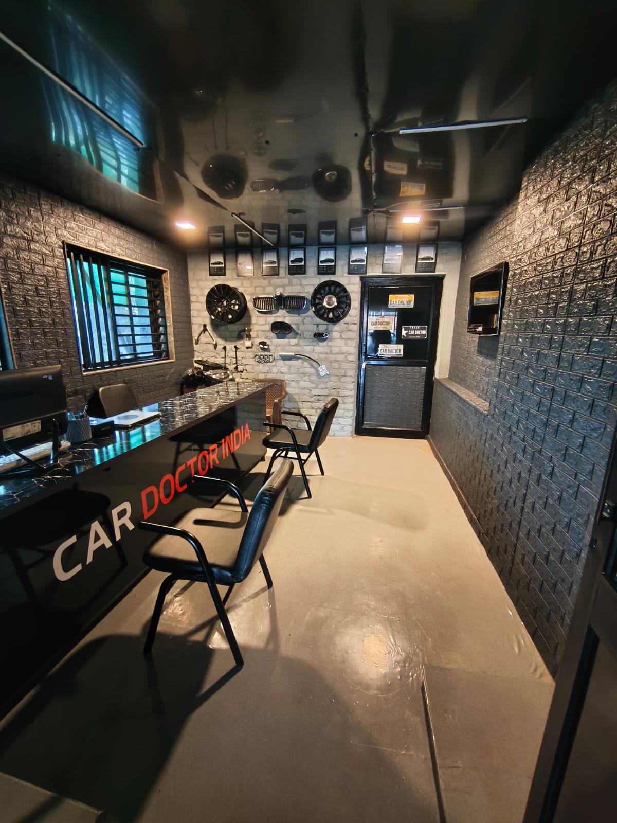 The Car Doctor India reception, with a branded desk and alloy wheels, grilles and performance parts displayed on the wall behind